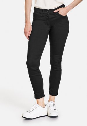 Schwarze, skinny Jeans aus Denim mit einer mittelhohen Taille, ausgestattet mit vorderen Taschen und einem nahtlosen Design. Kombiniert mit weißen Sneakern.