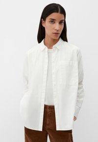Witte button-up shirt met een borstzak, gemaakt van lichtgewicht stof, gedragen over een licht top. Gecombineerd met bruine corduroy broek.