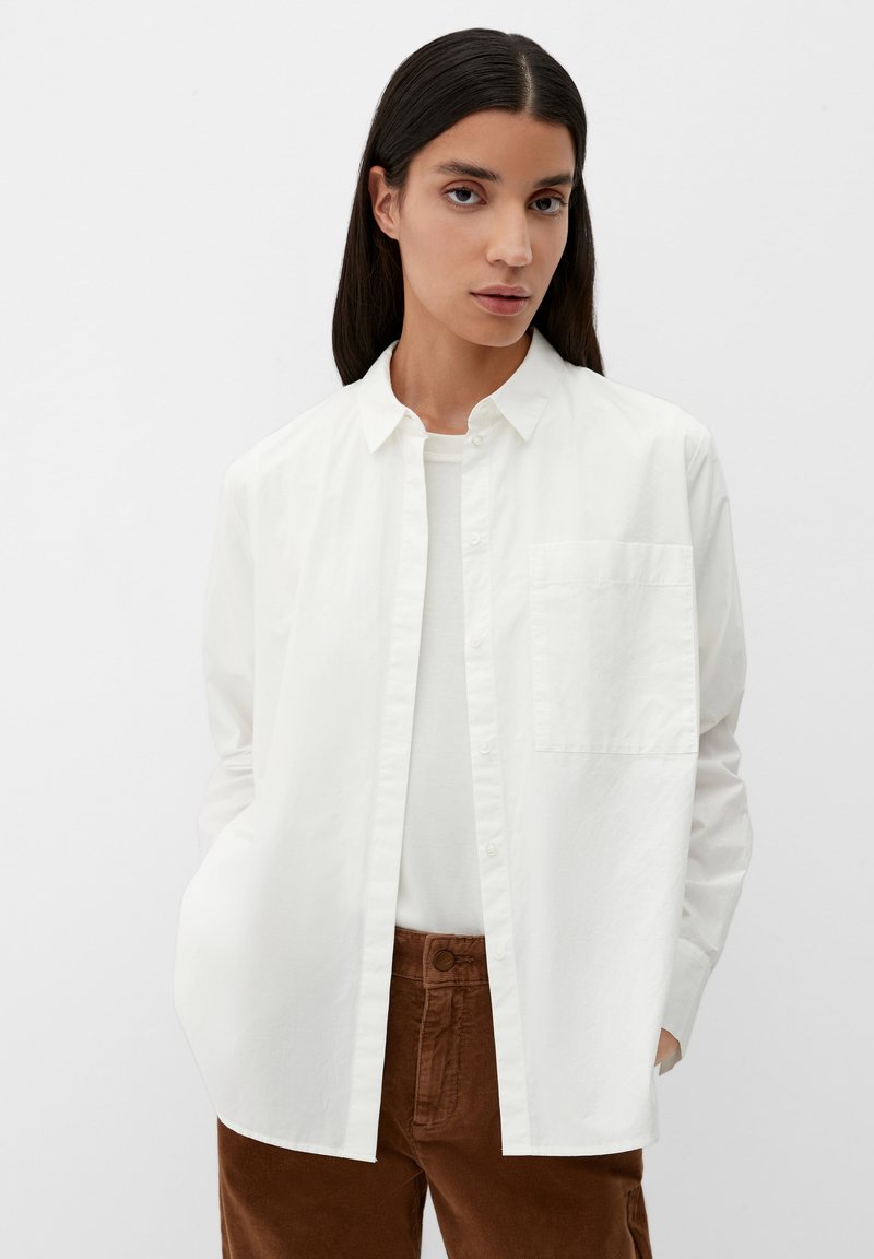 Witte button-up shirt met een borstzak, gemaakt van lichtgewicht stof, gedragen over een licht top. Gecombineerd met bruine corduroy broek.