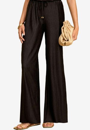 Pantaloni larghi neri con un motivo a zigzag testurizzato, vita elasticizzata e cordoncino. Abbinati a una pochette beige e sandali bassi.