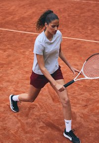 Grå sportt-shirt och vinröda shorts som bärs av en person som spelar tennis på röd lera. De håller en tennisracket och har på sig svarta skor med vita strumpor.