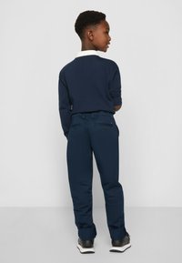 Marineblå langermet skjorte med hvit krage, kombinert med marineblå bukser med baklommer og svarte sneakers med hvite såler.