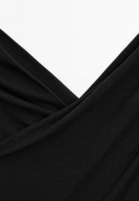 Sort stof med en blød, ribbet tekstur, prydet med draperede folder og et V-hals design, der skaber et lagdelt udseende.