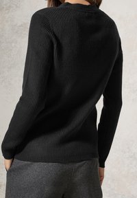 Schwarzer gerippter Strickpullover mit rundem Halsausschnitt, langen Ärmeln und taillierter Silhouette, kombiniert mit grauen Unterteilen. Glatte Textur.