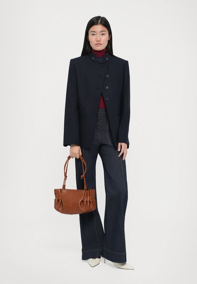 Marineblazer met knoopsluiting, gecombineerd met high-waisted donkere denim flares. Bruine leren tas met gatheringdetails. Witte spitse hakken.