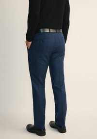 Granatowe spodnie w kratę z tkaniny tkanej, o prostym kroju, z tylnymi kieszeniami i eleganckim czarnym paskiem. Wygląd uzupełniają niskie czarne buty.