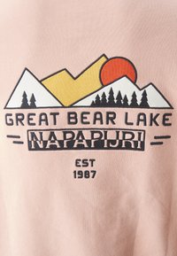 Tissu rose clair avec un motif graphique représentant des montagnes, un soleil et des arbres. Le texte inclut "Great Bear Lake" et "Napapijri", établi en 1987.