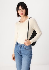 Suéter de punto color crema con un escote redondo, adornado con pequeñas cuentas. Combinado con jeans de talle alto de color azul claro y un bolso negro.