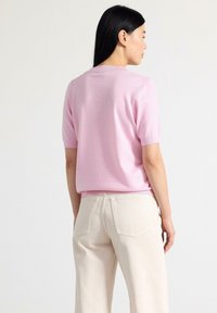 Maglione corto a maniche corte di colore rosa chiaro realizzato in materiale morbido, con un semplice scollo a giro e orlo a costine, abbinato a pantaloni beige pallido.