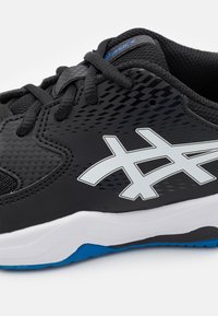 Botte de sport noire avec des panneaux en mesh, tige synthétique texturée, logo gris, semelle intermédiaire blanche et accents de semelle extérieure bleus.