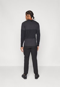 Ilgas rankovėmis juodas marškinėlis su tekstūruotu korpusu, derinamas su juodomis kelnėmis. Rinkinys pasižymi kontrastingais matiniais ir blizgiais audiniais.