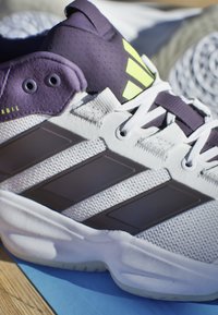 Sportsko i hvid, lilla og sort med mesh-overdel, tre sorte striber design og fremtrædende limegrøn accent på hælen.