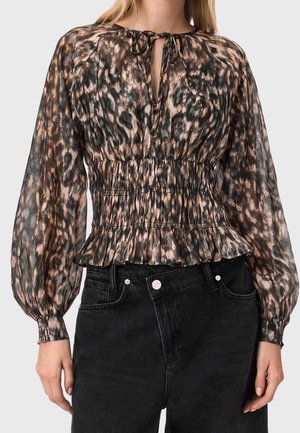 Kvinde har en langærmet leopardprint-bluse med bindebånd i halsen, raglanærmer, smocket talje og peplum, kombineret med høj taljede sorte jeans.
