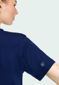 Námornícky modré tričko s krátkym rukávom vyrobené z mäkkého bavlneného materiálu. Obsahuje jemné logo vyšívané na ľavom rukáve. Okrúhly výstrih a voľný strih.