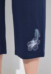 Pantaloni corti in cotone blu navy con vestibilità rilassata, caratterizzati da accenti floreali ricamati di colore blu chiaro sulla parte inferiore della gamba sinistra.