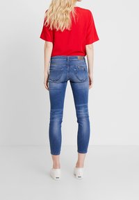 Vaqueros azules de corte ajustado, con cintura media y bolsillos traseros cosidos. Combinados con una blusa roja suelta y calzado blanco.