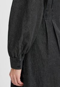 Robe en denim noir au style décontracté, avec des manches bouffantes, des poignets boutonnés et des détails plissés dans le dos. Design texturé et décontracté.