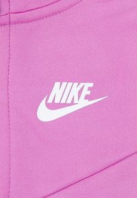 Pinkfarbener sportlicher Stoff mit einem weißen Nike-Logo. Die Textur wirkt glatt mit einer sauberen Nahtverarbeitung.