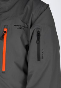 Grijze waterdichte jas met oranje ritsaccenten, voorzien van een ritszak op de mouw en "STX 20.000" gedrukt op de arm.
