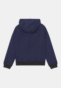 Námořnická modrá lehká bunda s kapucí, elastickými manžetami a černým lemem. Hladký, voděodolný materiál s jednoduchým designem.