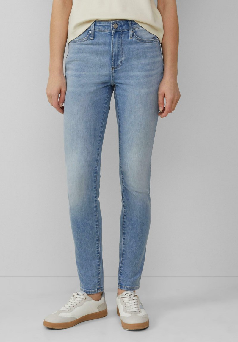 Jean skinny bleu clair en denim, avec une taille mi-haute, des poches avant et un léger délavage sur les cuisses, associés à des baskets blanches.