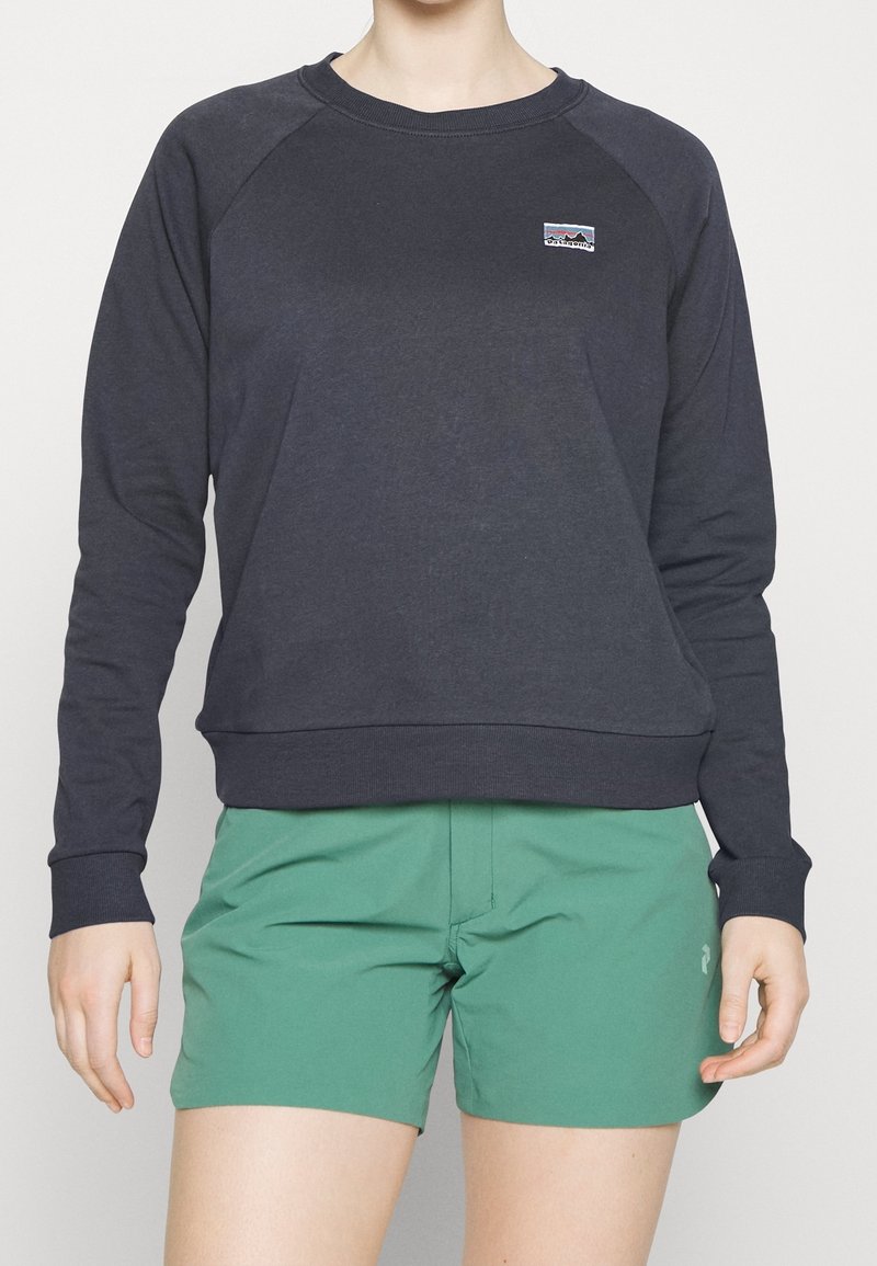 Sudadera de color azul marino oscuro con cuello redondo y mangas raglán, combinada con pantalones cortos verdes. Presenta un pequeño logo en el pecho. Textura de tela suave.