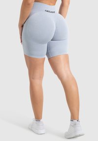 Grijze sportshorts van rekbaar materiaal met een hoge tailleband, voorzien van een logo aan de achterkant en een gladde textuur. Gedragen met witte sneakers.