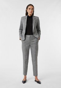 Grijze textuur blazer met bijpassende op maat gemaakte broek, gecombineerd met een zwarte coltrui en zwarte slingback ballerina's. Strakke lijnen en moderne pasvorm.