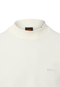 Witte geribde coltrui gemaakt van stof, met een subtiele geborduurde "BOSS"-logo op de voorkant en een hoge, strakke kraag.
