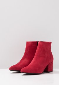 Bottes cheville en daim rouge avec un bout pointu et un talon bloc. Elles présentent une fermeture éclair latérale et une finition à texture lisse.