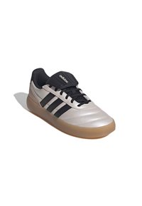 Zapatillas de fútbol plateadas con detalles en negro, que cuentan con una parte superior sintética lisa, cierre de cordones y una suela de goma color chicle para tracción.