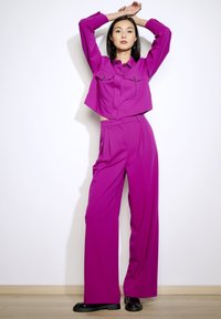 Fuchsia cropped shirt with chest pockets and wide-leg trousers, both in smooth fabric, paired with black platform shoes.
