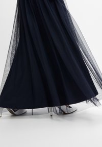 Sjöblå tylkjol med lagerstruktur och genomskinlig design. I sällskap av silverhöga klackar med spetsig tå.