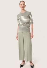 Gestreifter Strickpullover in Grau und Creme, kombiniert mit weiten hellgrünen Hosen. Schwarze spitze Schuhe mit Knöchelriemen.