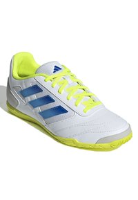 Zapatilla deportiva blanca con diseño de tres franjas azules, acentos en amarillo brillante, lengüeta de malla texturizada y suela de goma para agarre.