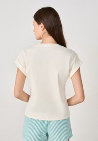 Top corto de canalé crema con mangas enrolladas, que presenta un corte relajado y un escote redondeado, combinado con pantalones cortos a rayas en verde menta.