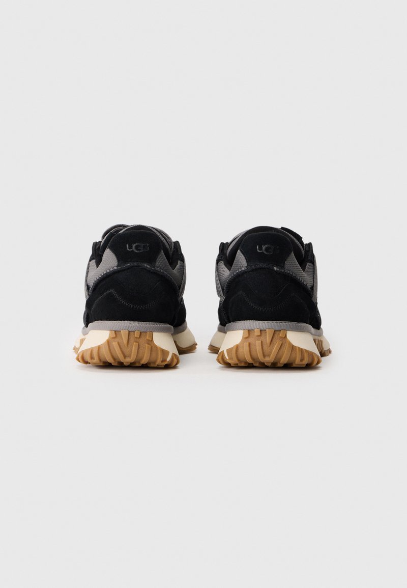 Baskets de sport noires et grises avec une tige en daim et en mesh, dotées d'une semelle en caoutchouc avec un motif texturé. Logo sur le talon.