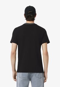 T-shirt nero a maniche corte con dettagli del colletto bianco a contrasto, abbinato a jeans azzurri, visto da dietro.