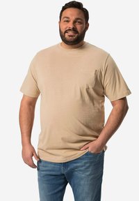 Beige tričko s krátkým rukávem, s přední kapsou, kulatým výstřihem a měkkou texturou, spárované s modrými džínami.