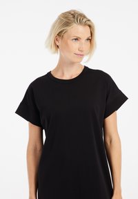 Czarna sukienka T-shirt z krótkimi, zwiniętymi rękawami i klasycznym okrągłym dekoltem. Wykonana z gładkiego materiału, charakteryzuje się luźnym krojem i minimalistycznym stylem.