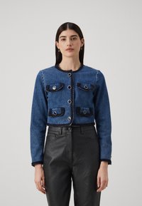 Jachetă din denim cu patru buzunare, feronerie aurie și cusături în contrast. Lungime scurtă, din țesătură albastră cu un trim texturat negru.
