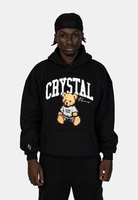 Zwarte hoodie met een grote graphic van een teddybeer die een shirt draagt met "Crystal Paris", voorzien van een voorzak en ribgebreide manchetten.