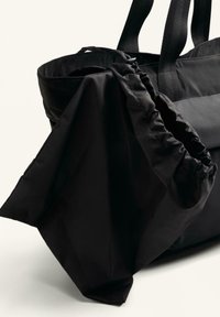 Fekete szövet bevásárlótáska húzózsinóros, összehúzható rekeszel, masszív pántokkal és sima felülettel. Minimalista kialakítás.