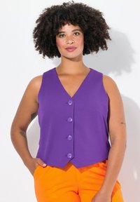 Gilet viola senza maniche con scollatura a V, caratterizzato da quattro bottoni tondi e un orlo leggermente curvato, abbinato a pantaloni arancioni.