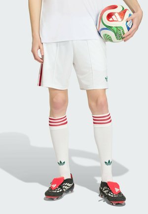 Person, der holder en flerfarvet fodbold, iført hvide shorts, hvide knæstrømper med røde striber og sorte fodboldstøvler med røde detaljer.