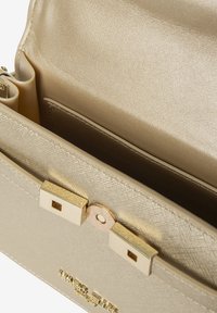 Gouden handtas met een gestructureerde textuur en een glad interieur, voorzien van een veilige sluiting, meerdere vakken en subtiele branding aan de voorkant.