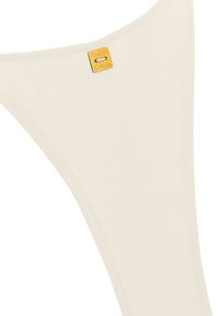 String beige realizzato in morbido tessuto, con una superficie liscia e un piccolo etichetta in metallo dorato con scritta in rilievo.