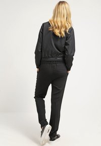 Czarny sportowy dres z dopasowaną, zapinaną na zamek kurtką z prążkowanymi mankietami oraz dopasowanymi spodniami z elastycznym paskiem. Gładka, matowa tekstura.