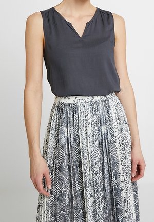 Haut sans manches gris foncé avec encolure en V, associé à une jupe blanche fluide ornée d'un imprimé peau de serpent noir et d'un design plissé.