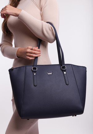 Navy blue tote bag made of textured material, featuring two long handles and silver hardware accents, rectangular shape, and a logo detail.